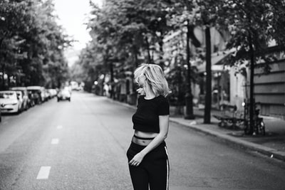 一个女人靠在后面站在街上的灰度照片
